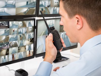 Male Security Guard Talking On Walkie-talkie Close-up Of Male Security Guard Talking On Walkie-talkie While Monitoring Multiple CCTV Footage